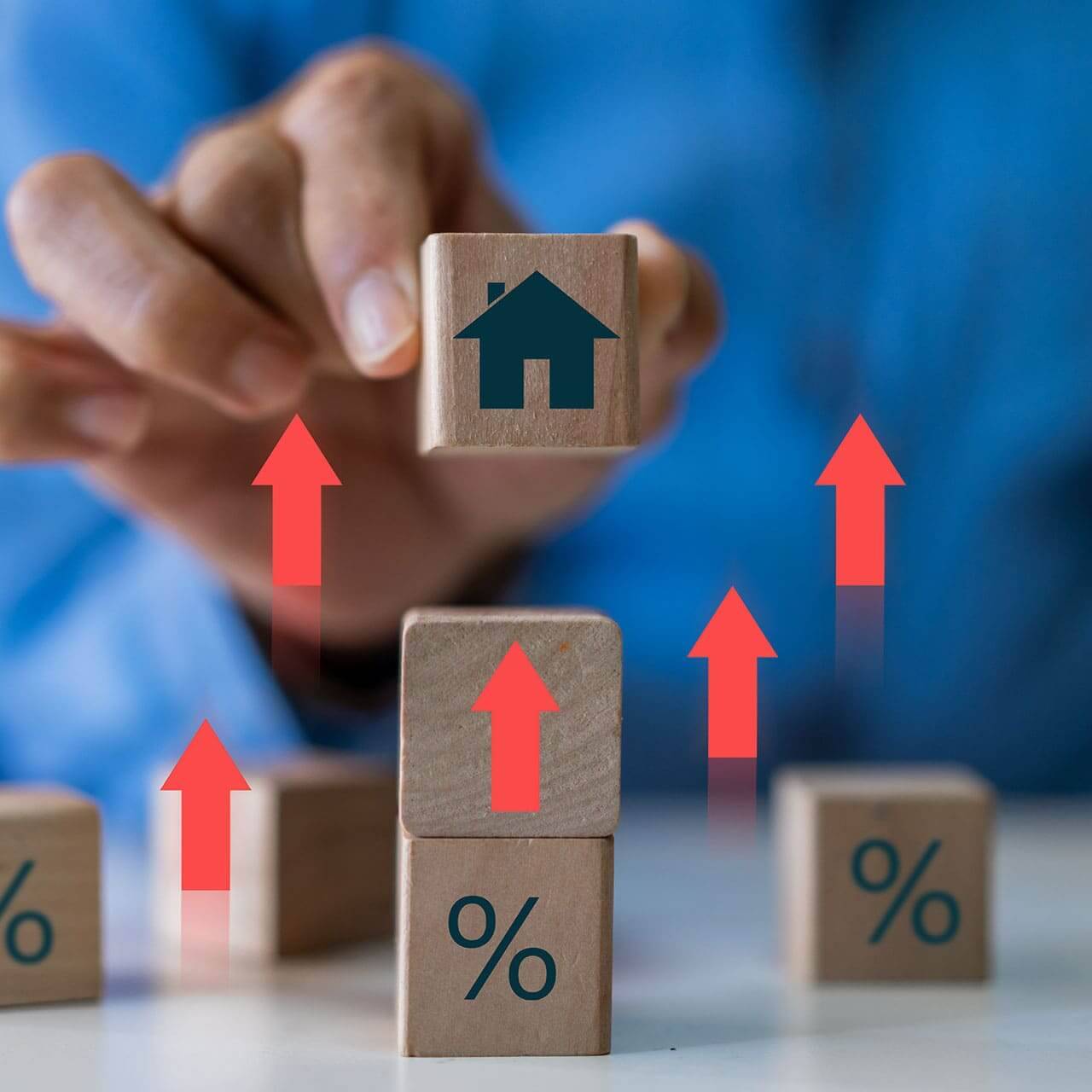 Person mit Holzwürfeln, Prozentzeichen und Haus als Symbolbild für die Immobilienpreise in Lützen